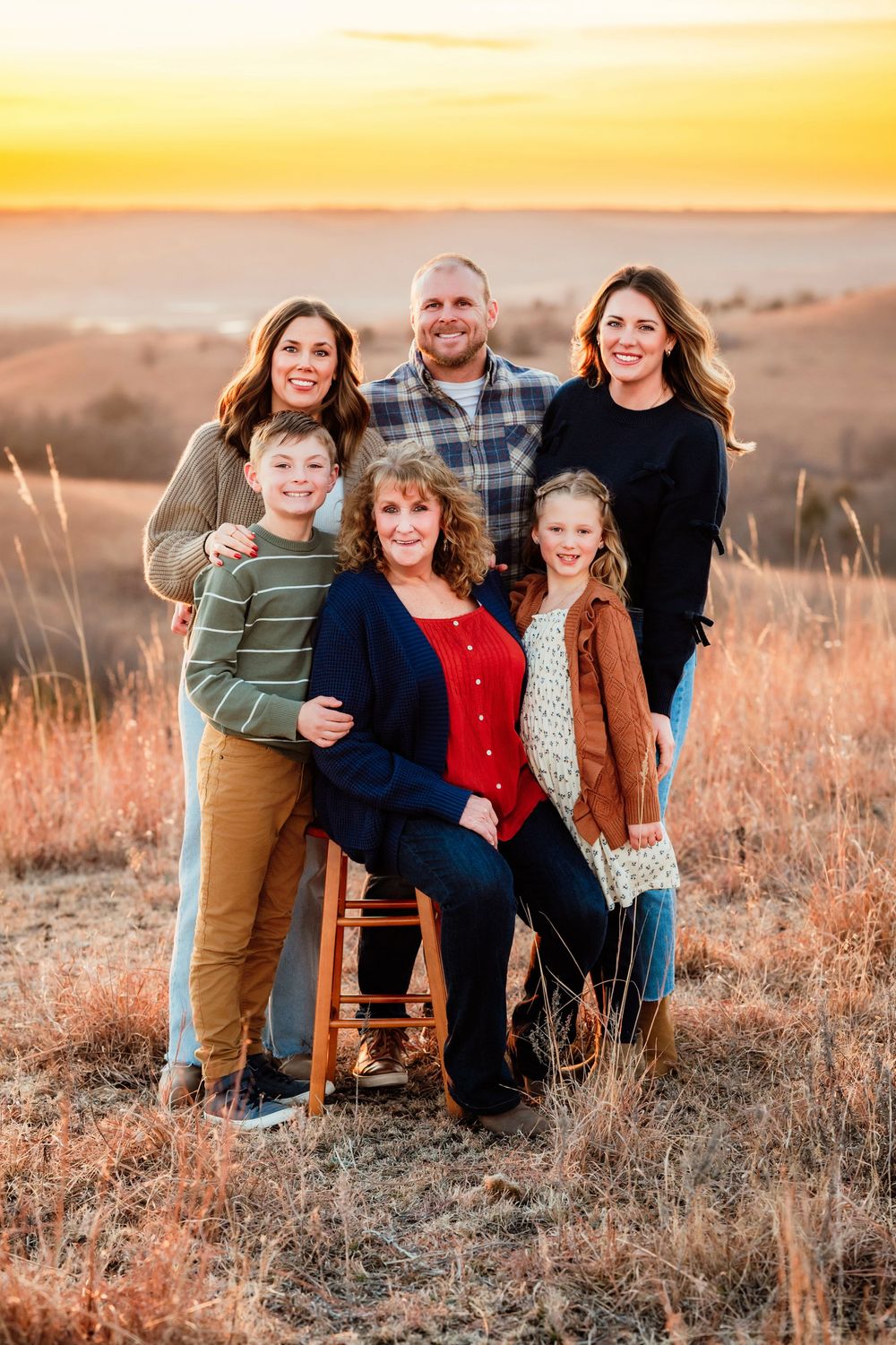 Family portrait session at golden hour in a grassy field with warm sunset lighting.