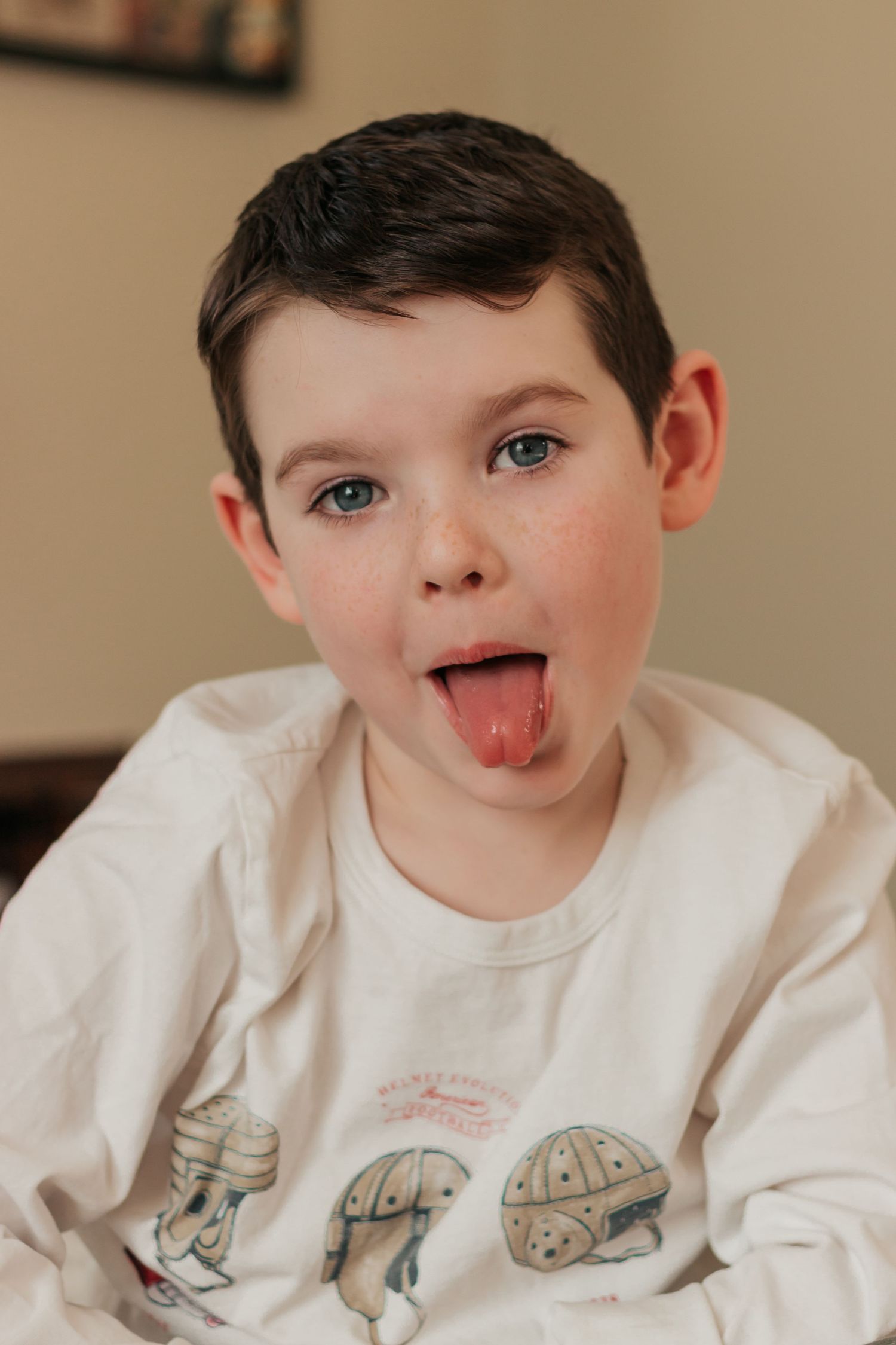 Young boy with dark hair and blue eyes sticking his tongue out, wearing a white graphic t-shirt. | Annual Birthday Photos for Kids