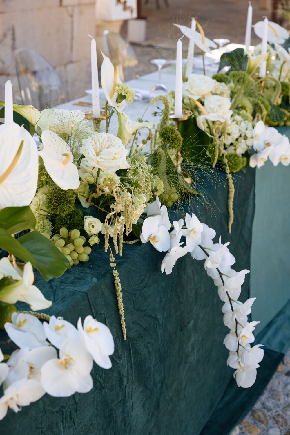 Elegant white floral centerpiece with orchids, roses and candles on a dark green tablecloth.