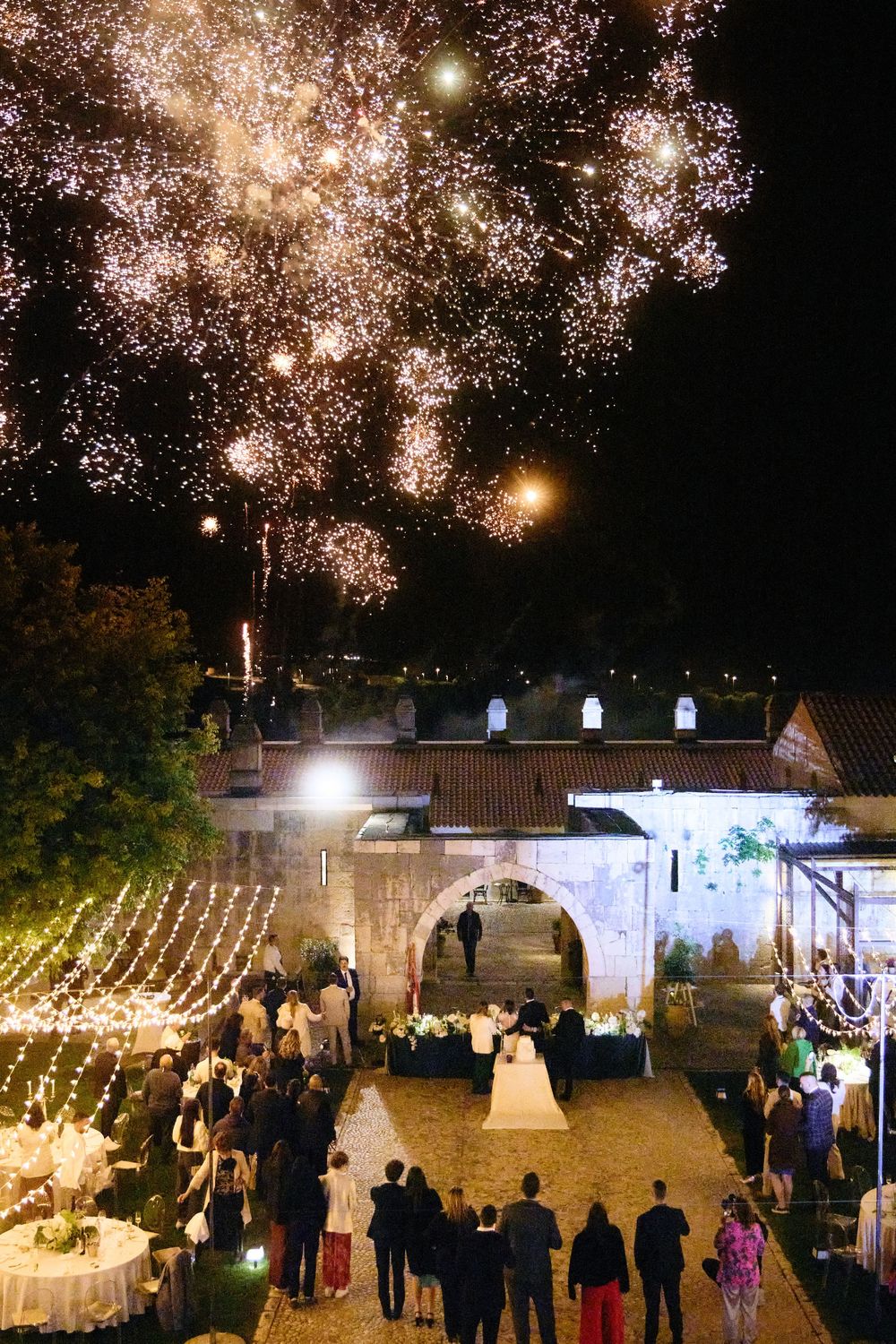 Spectacular fireworks display over an illuminated courtyard during an evening celebration.
