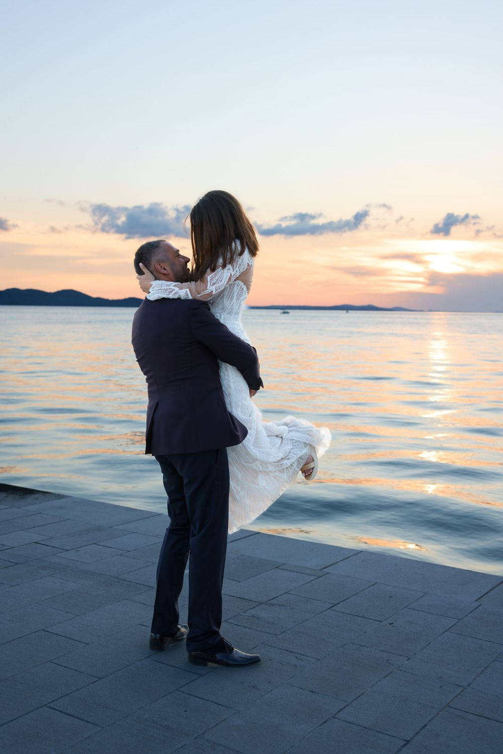 Newlyweds embrace against a sunset ocean backdrop on their wedding day.