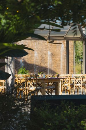 Outdoor restaurant patio with wooden chairs and tables set against a brick wall in dappled sunlight.