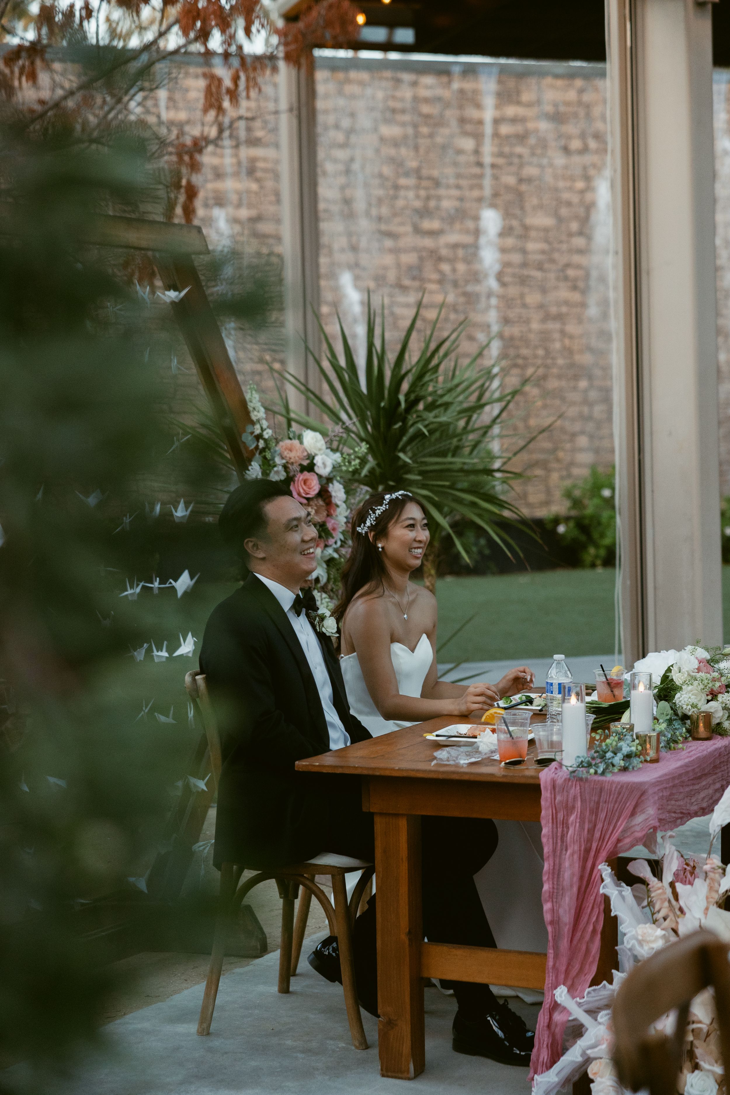 Wedding reception table with pink runner and floral arrangements in a rustic venue with brick walls and greenery.