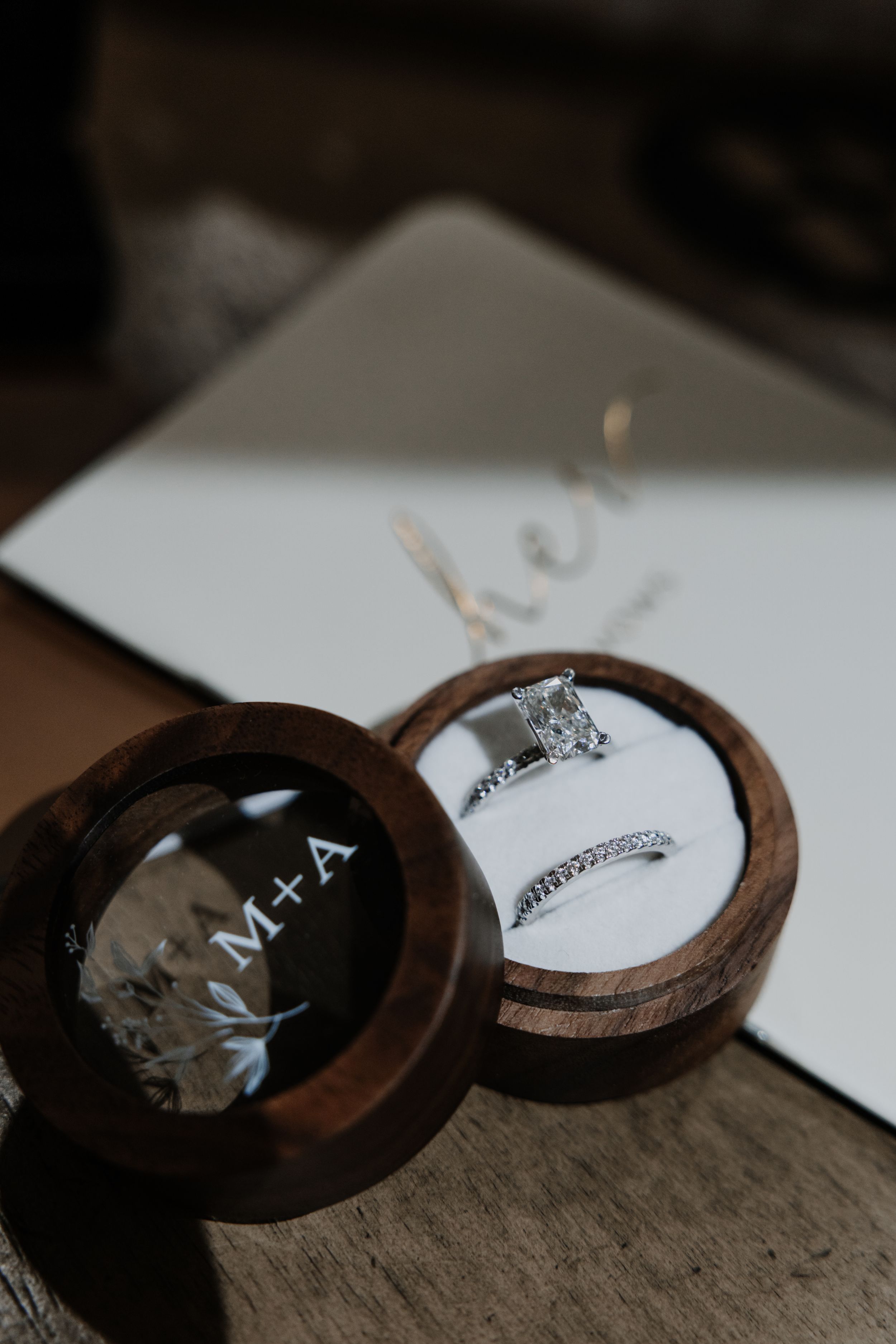 Wedding rings displayed in a wooden ring box with engraved details on a white surface.
