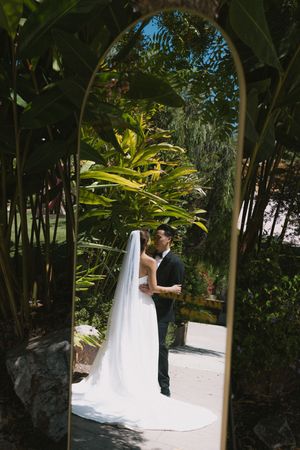 A couple shares a romantic moment in a lush tropical garden setting during their outdoor wedding ceremony.