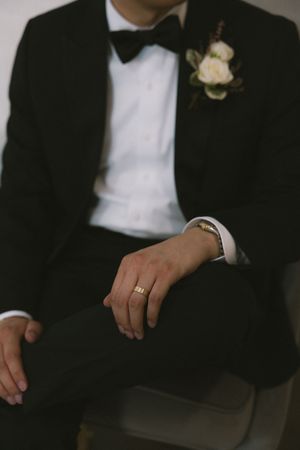 Close-up view of hands wearing black tuxedo sleeves and white cuffs showing wedding rings and boutonniere.