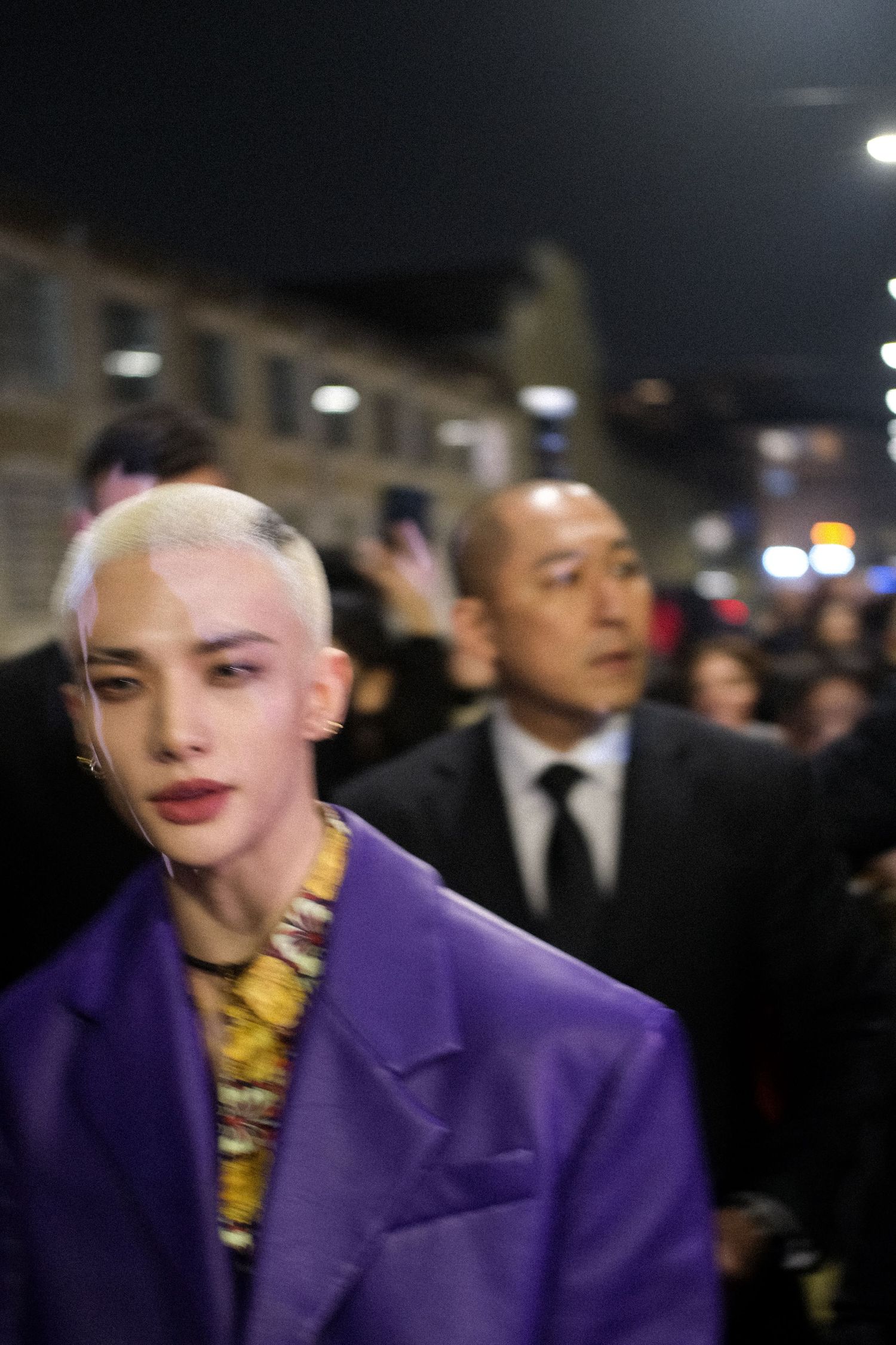 A person wearing a vibrant purple coat and gold necklace is seen at a formal evening event.