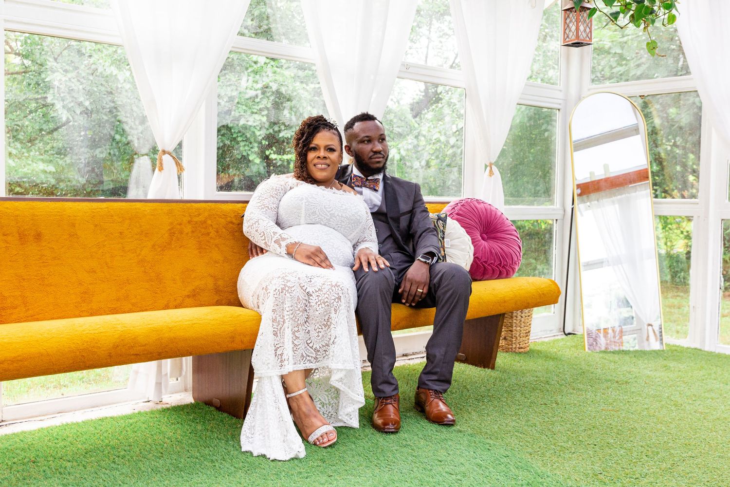 A couple sits together on a yellow bench during an outdoor photoshoot in a garden setting.