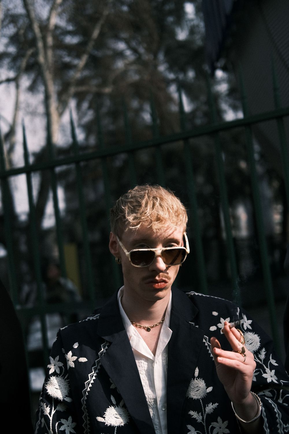 A figure in a black studded jacket stands in a dark forest setting with sunlight filtering through the trees.