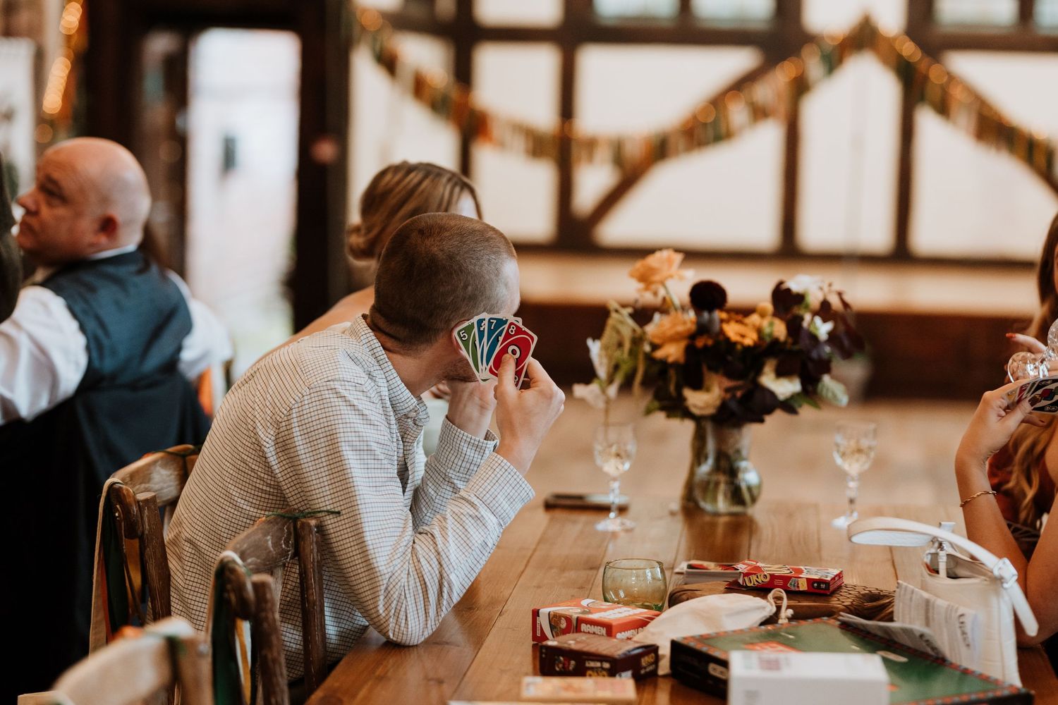 People dining at a rustic restaurant with wooden beams and floral centerpieces on the tables playing Uno during drinks reception