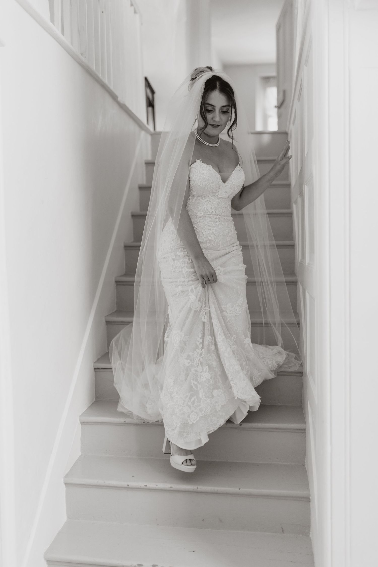 A bride in a white lace wedding dress walks up elegant white stairs in a sequence of artistic bridal portraits at Lyde Court, Hereford