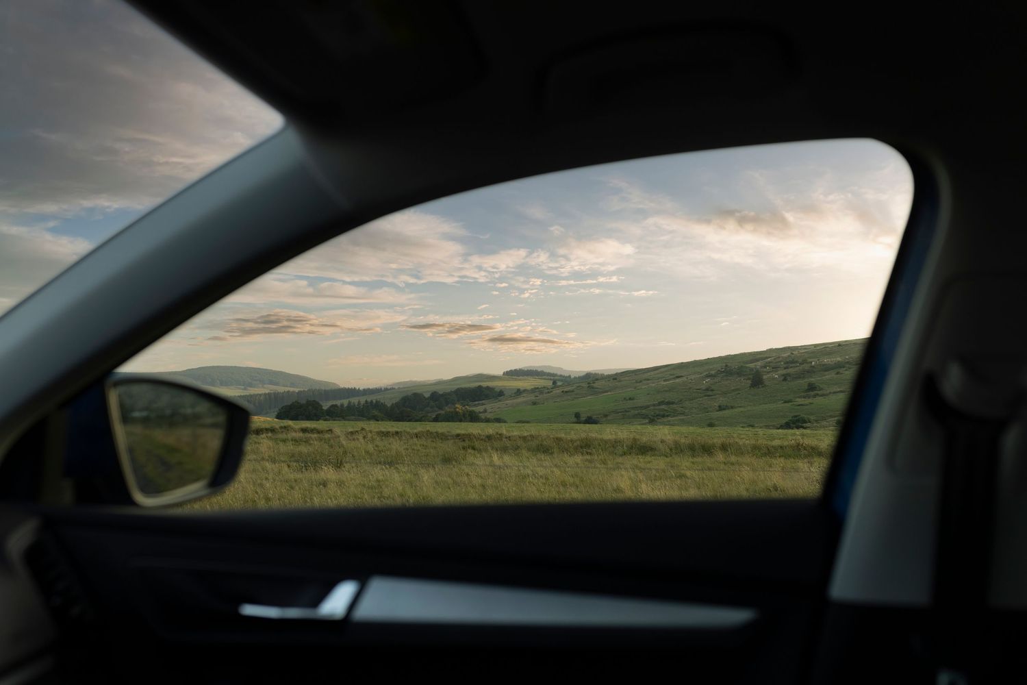 Paysage de collines au coucher du soleil aperçu à travers la vitre latérale d'une voiture moderne, illustrant le voyage et la liberté lifest