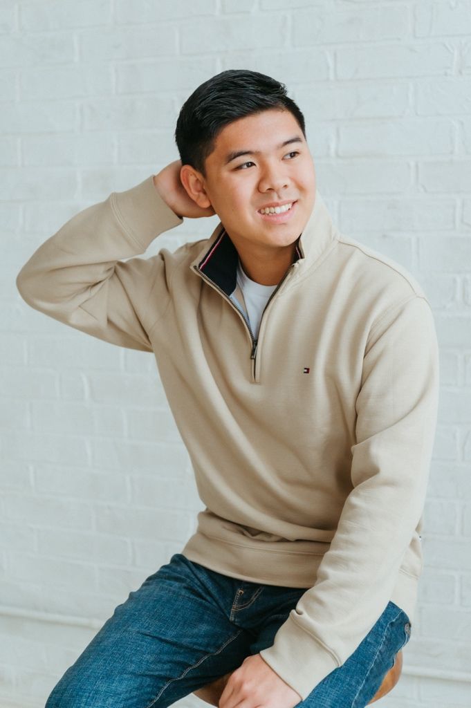 Person wearing cream quarter-zip sweater and blue jeans poses casually against white wall in lifestyle photoshoot.
