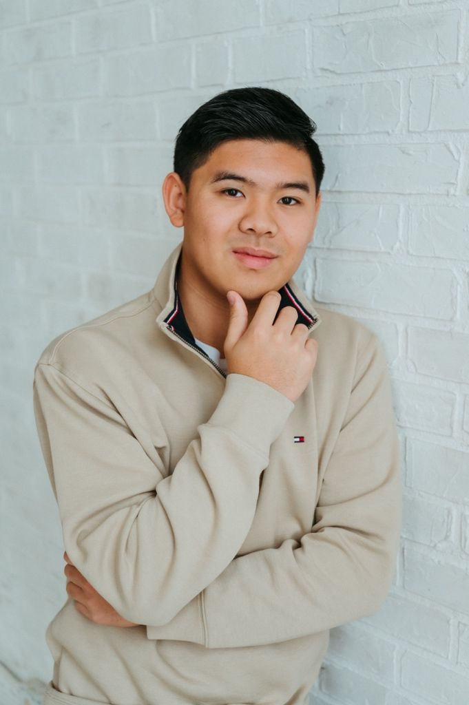 Person in casual beige sweater poses thoughtfully against white wall.