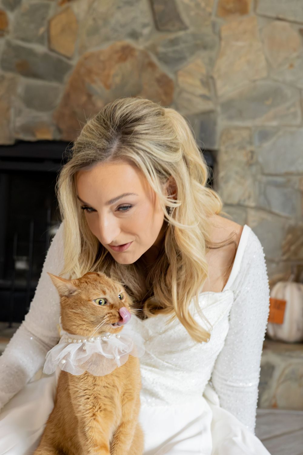 A person in a white lace top poses with an orange tabby cat against a stone wall background.