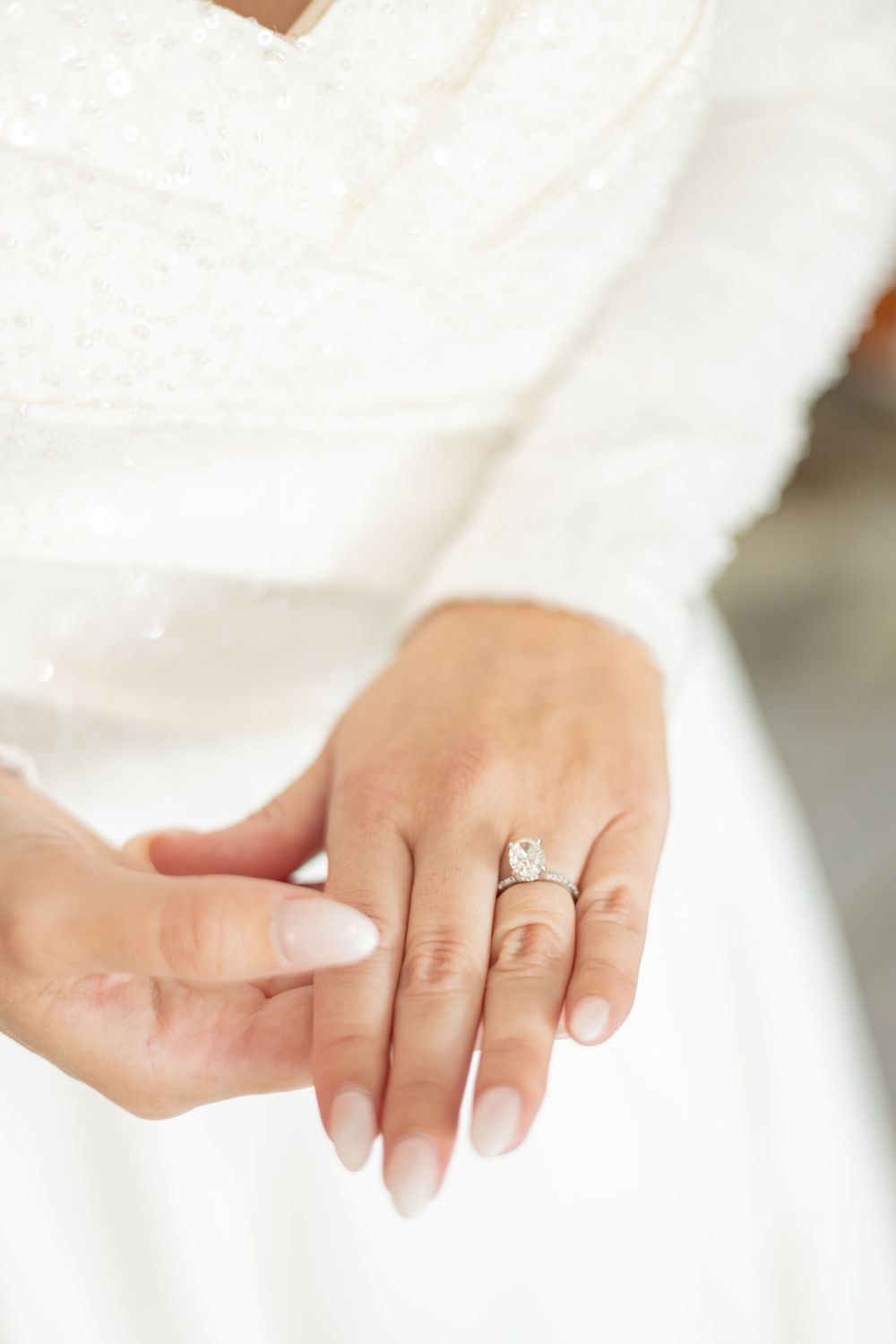Close-up view of a sparkling diamond engagement ring on a hand wearing a white dress.