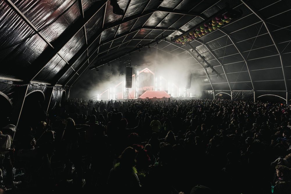 A dark concert venue filled with a large crowd watching a performance under dramatic lighting.