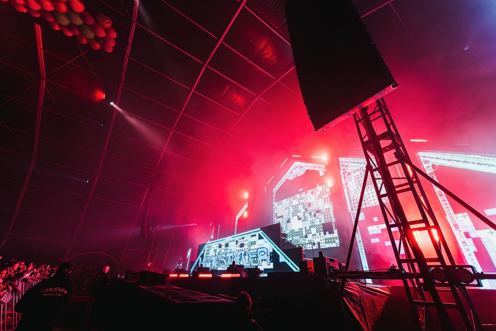 Concert stage illuminated with dramatic red lighting and video screens during a live performance at an indoor venue.