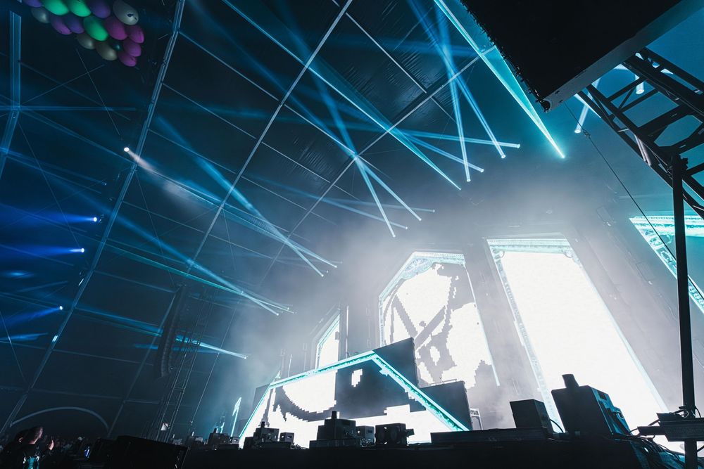 Concert venue illuminated with dramatic blue lighting and laser beams creating an atmospheric nightclub environment.