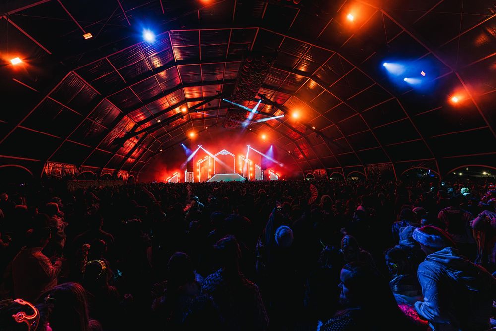 Crowd silhouettes at a nightclub with colorful red and blue lighting illuminating an arched ceiling during a performance.