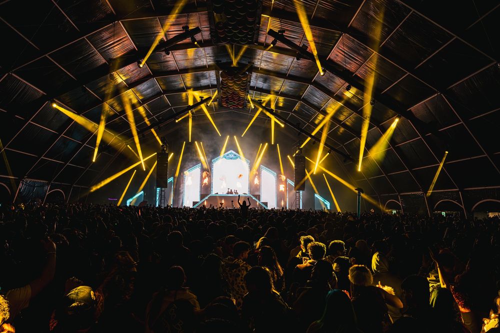 Concert crowd illuminated by bright yellow stage lights during an energetic performance at a music venue.