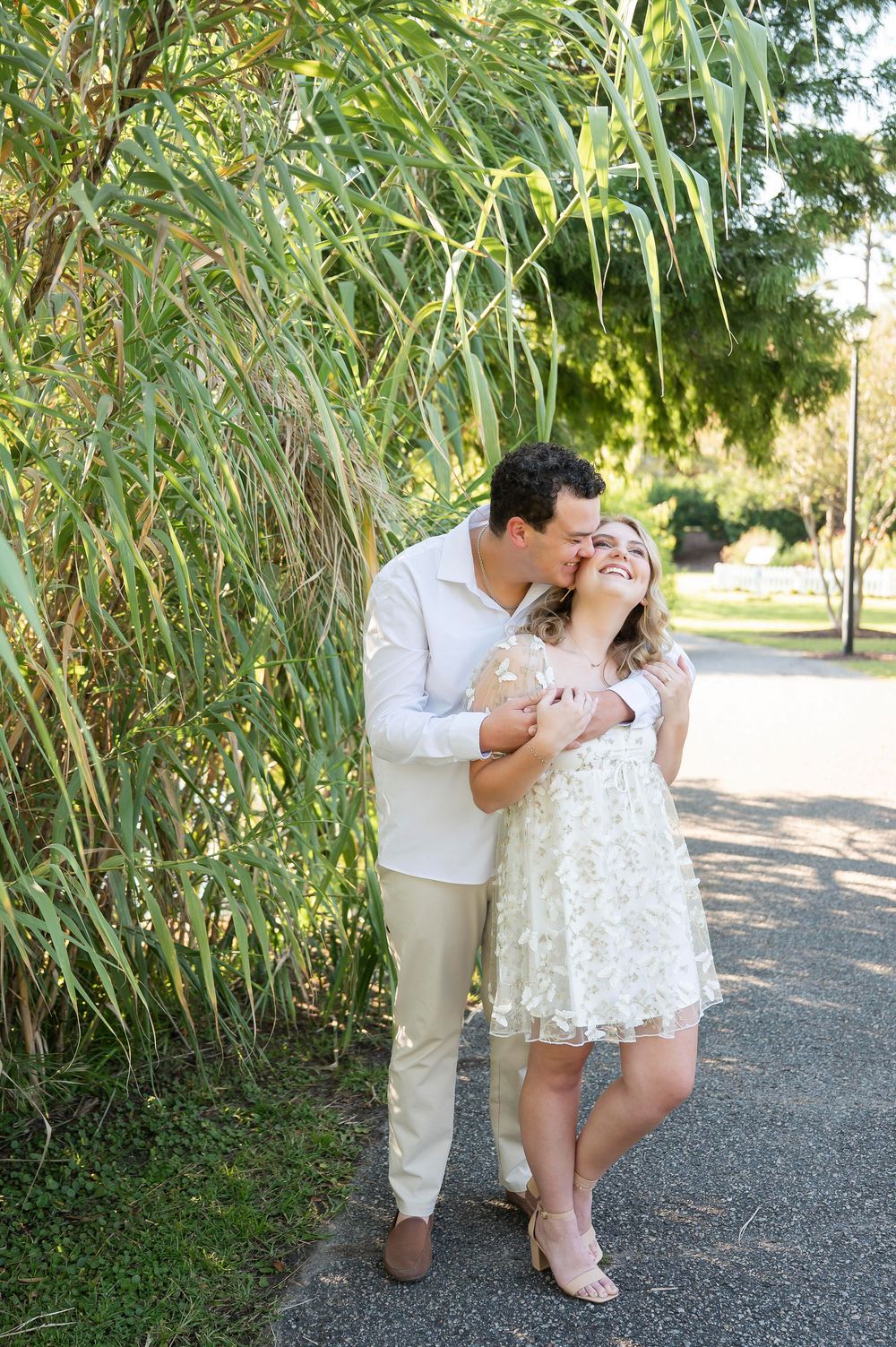 A couple shares tender moments near tall grass during a sunny outdoor photoshoot.