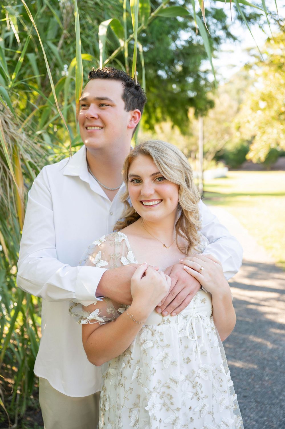 A couple laughs together during their engagement session near bamboo plants.