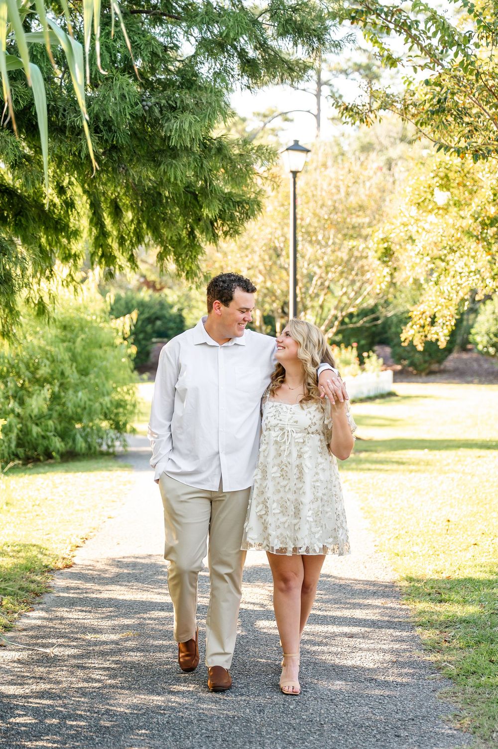 A couple walks together on a tree-lined path during golden hour.