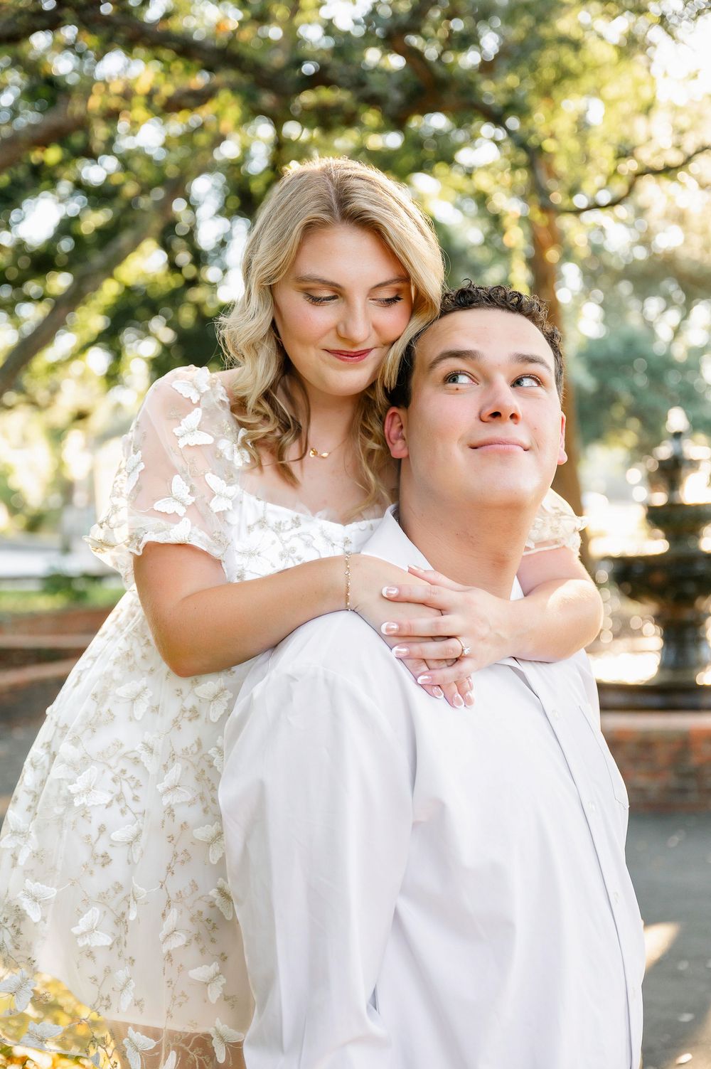 A couple shares an intimate embrace while posing for engagement photos in a park setting.