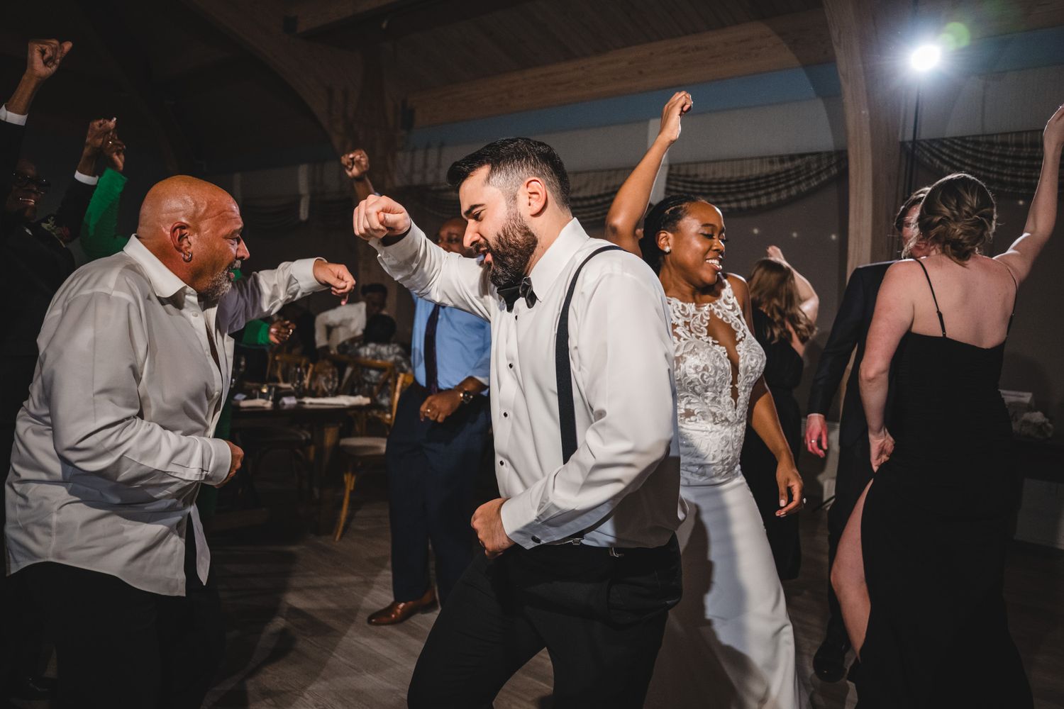 Wedding reception dance floor filled with guests dancing and celebrating in dark ambient lighting.