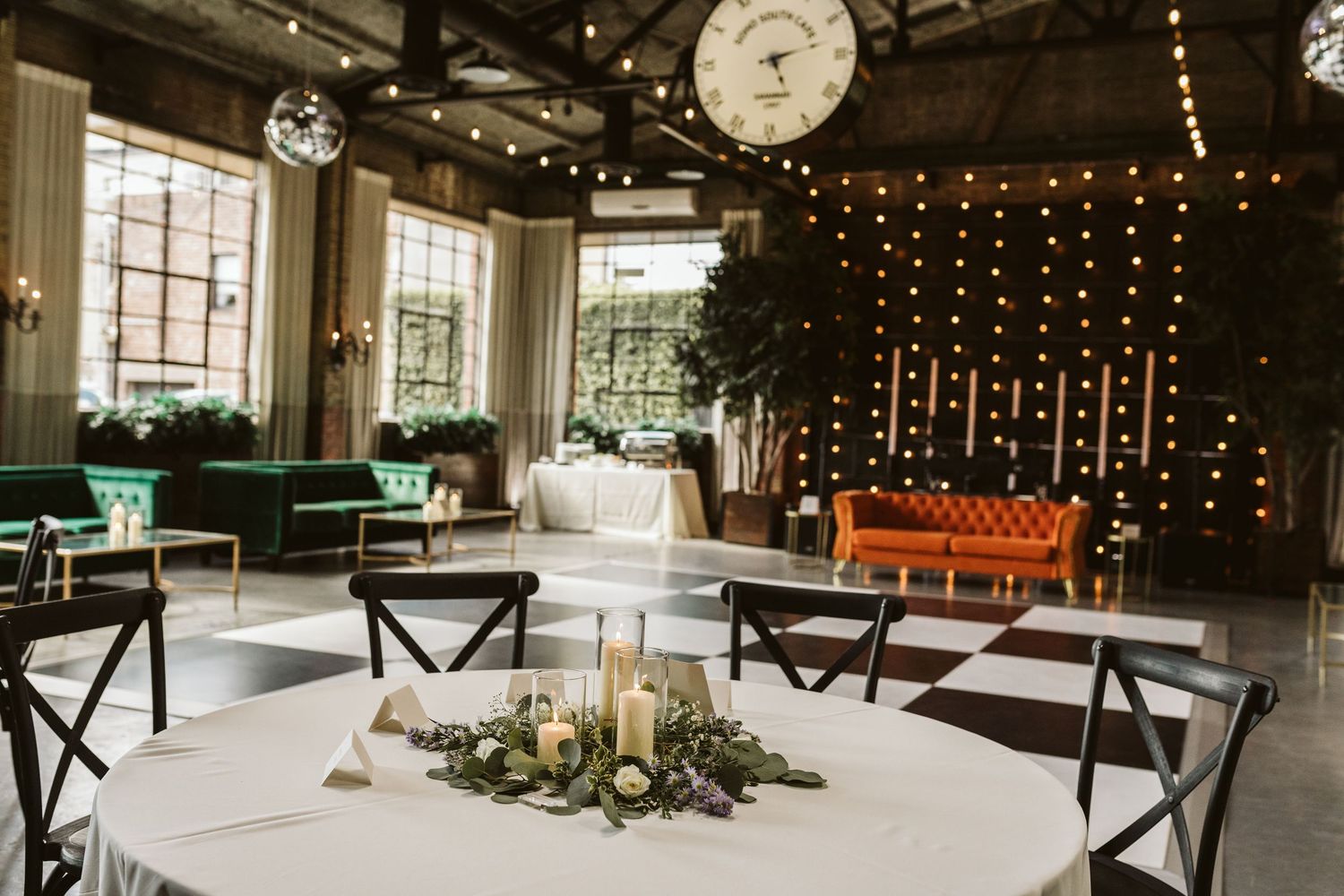 Modern event space with string lights, green seating, and floral centerpiece.