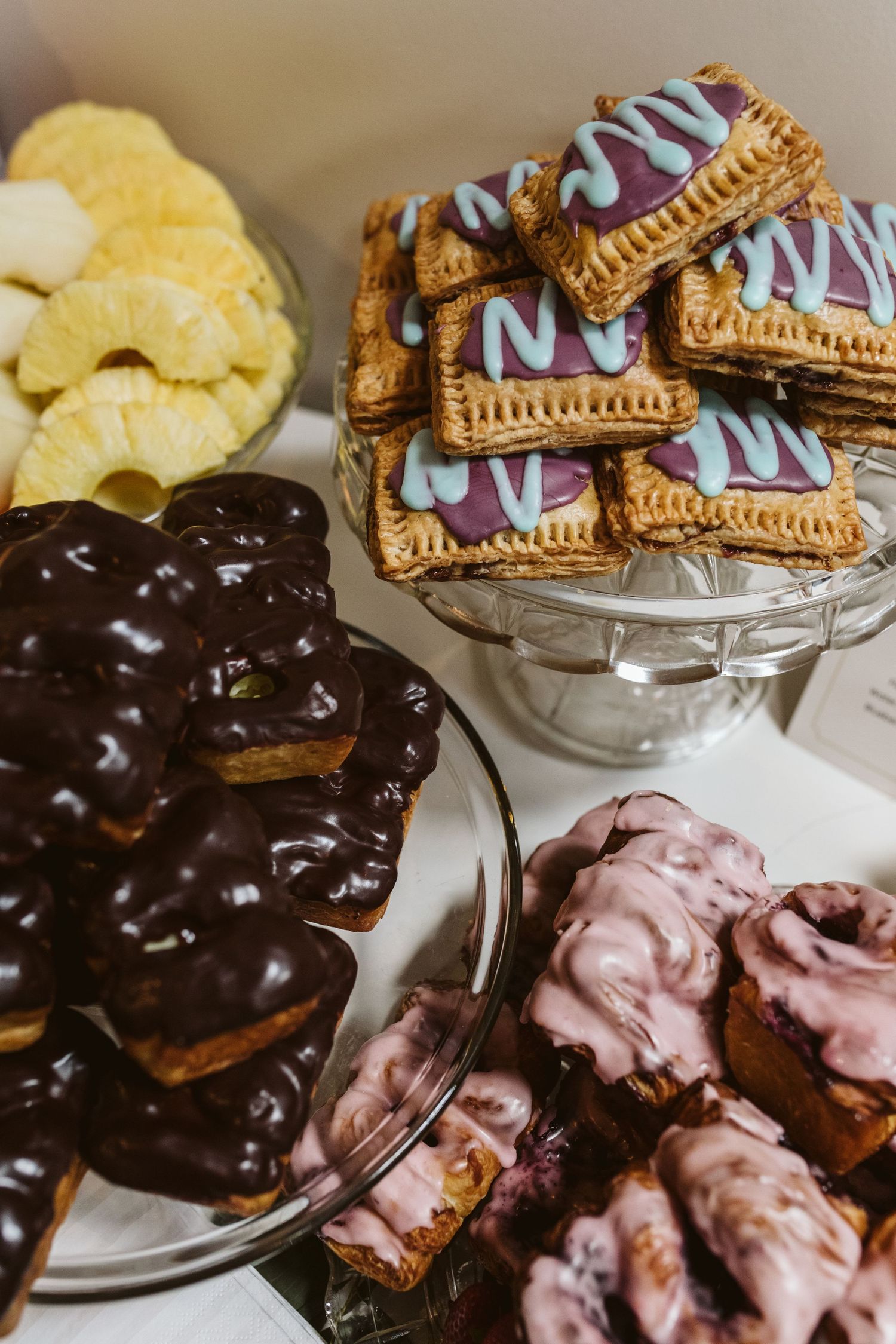 Dessert table featuring chocolate-covered pastries and decorated cookies on glass stands.