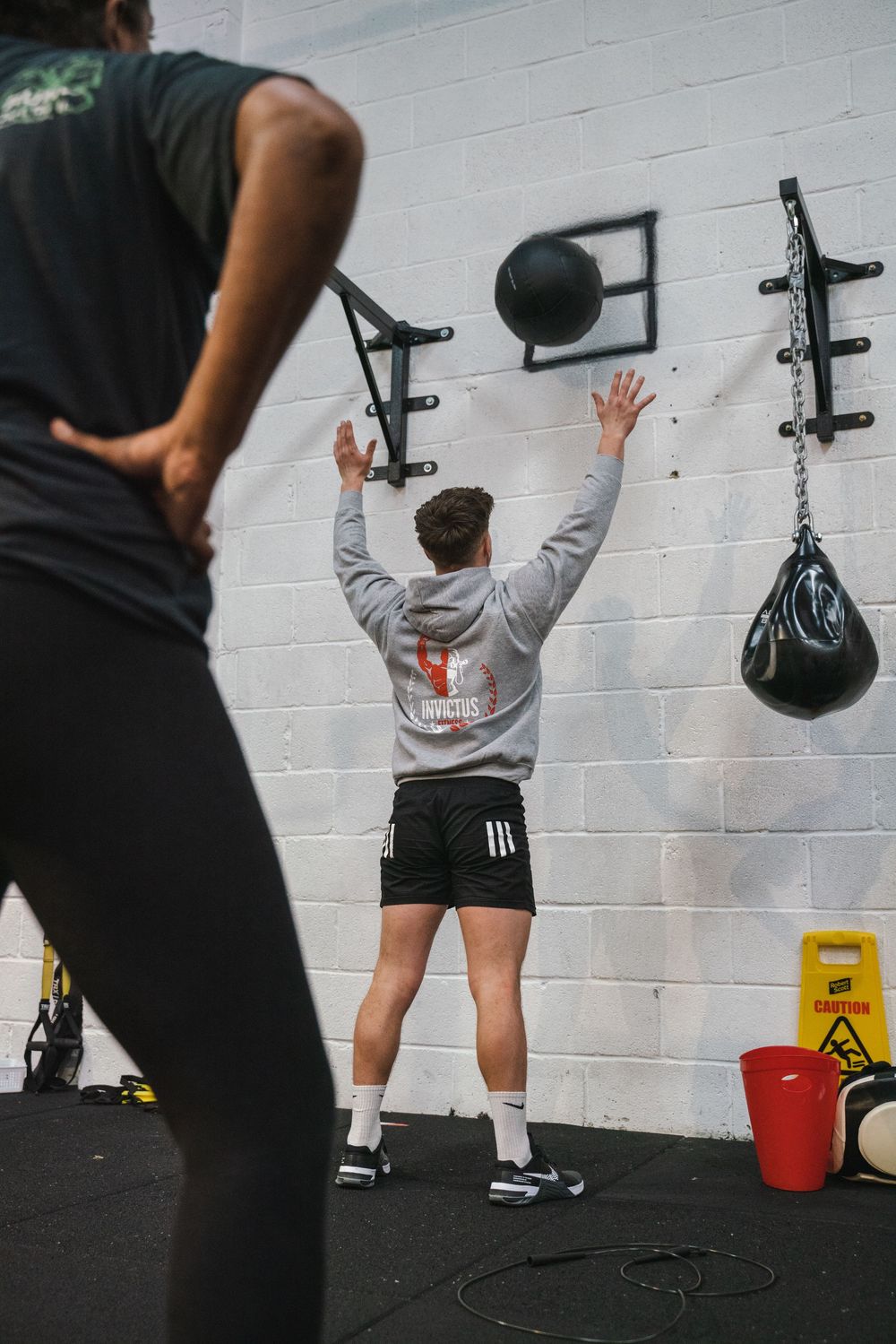 Fitness enthusiast performing wall ball exercises while trainer observes form.