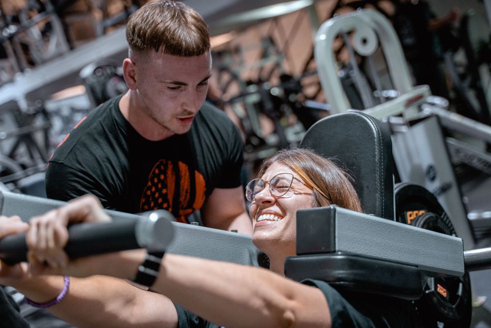 Personal trainer assists client with proper form during a weight machine exercise at the gym.