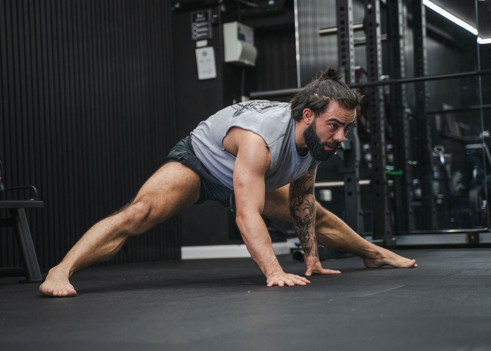Fitness enthusiast doing bodyweight exercises on a dark gym floor with fluorescent lighting.