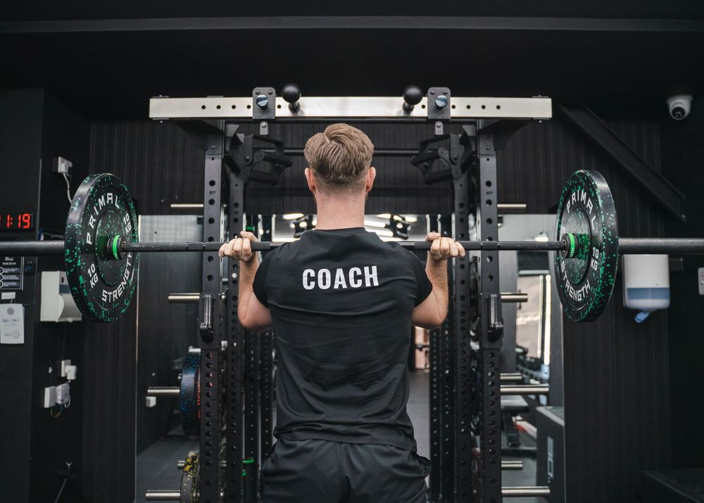 Back view of fitness instructor standing in front of weight training equipment in dark gym.