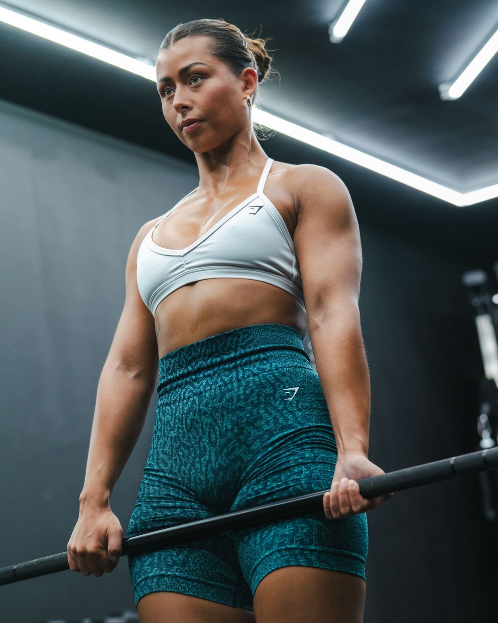 Athlete in teal shorts and sports bra grips a barbell during strength training.
