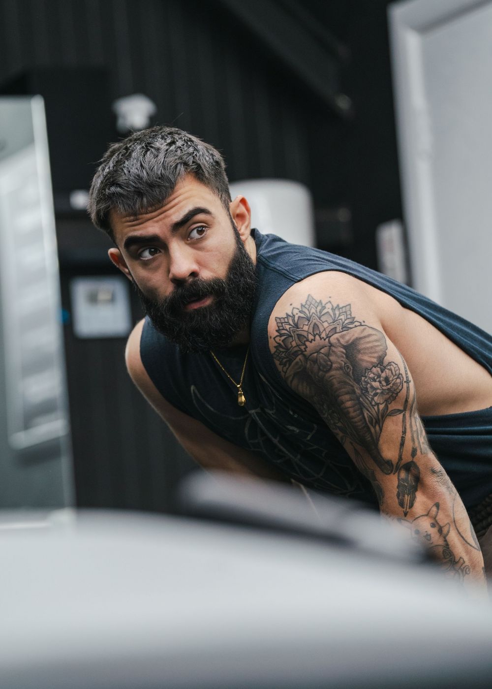 Tattooed man in tank top leaning forward during gym workout session.