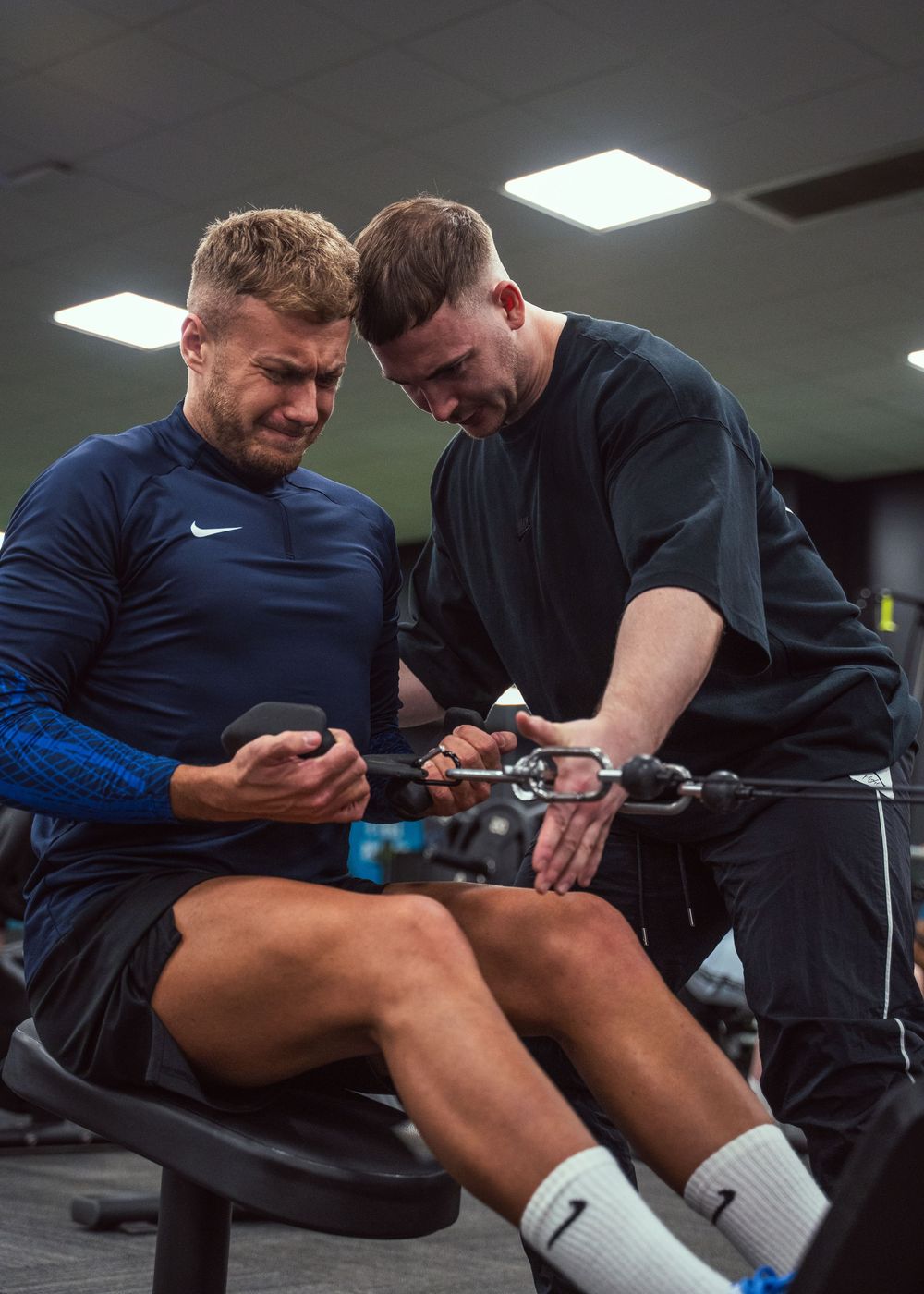 Two individuals reviewing fitness data or workout plan while seated at gym equipment.
