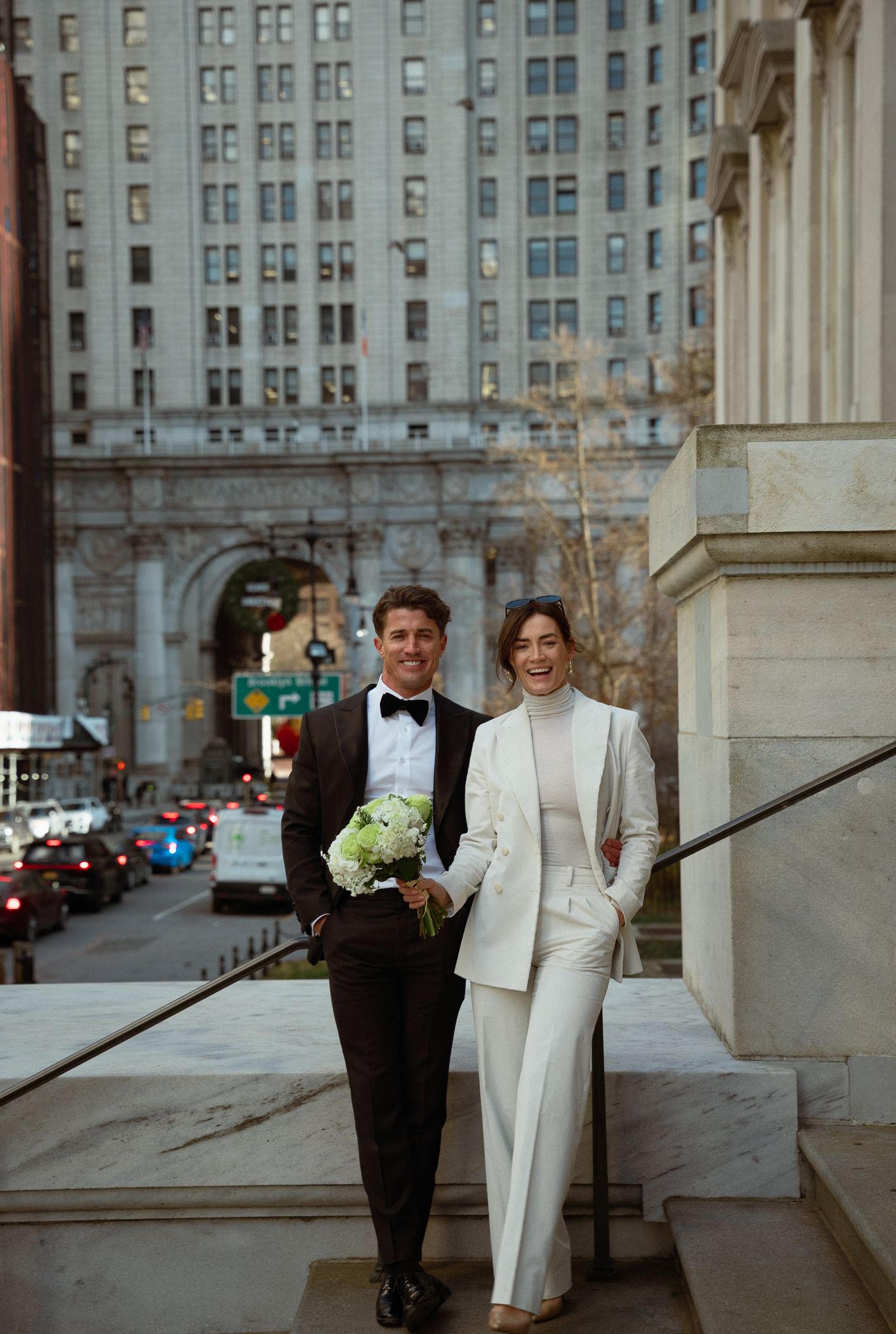 A couple poses elegantly against a backdrop of classic architecture and city buildings.