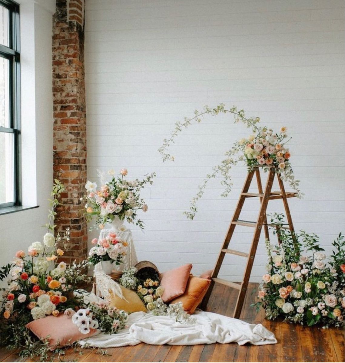 Romantic wedding backdrop with wooden ladder, flowing white fabric, and peach roses against white walls and patterned rug.