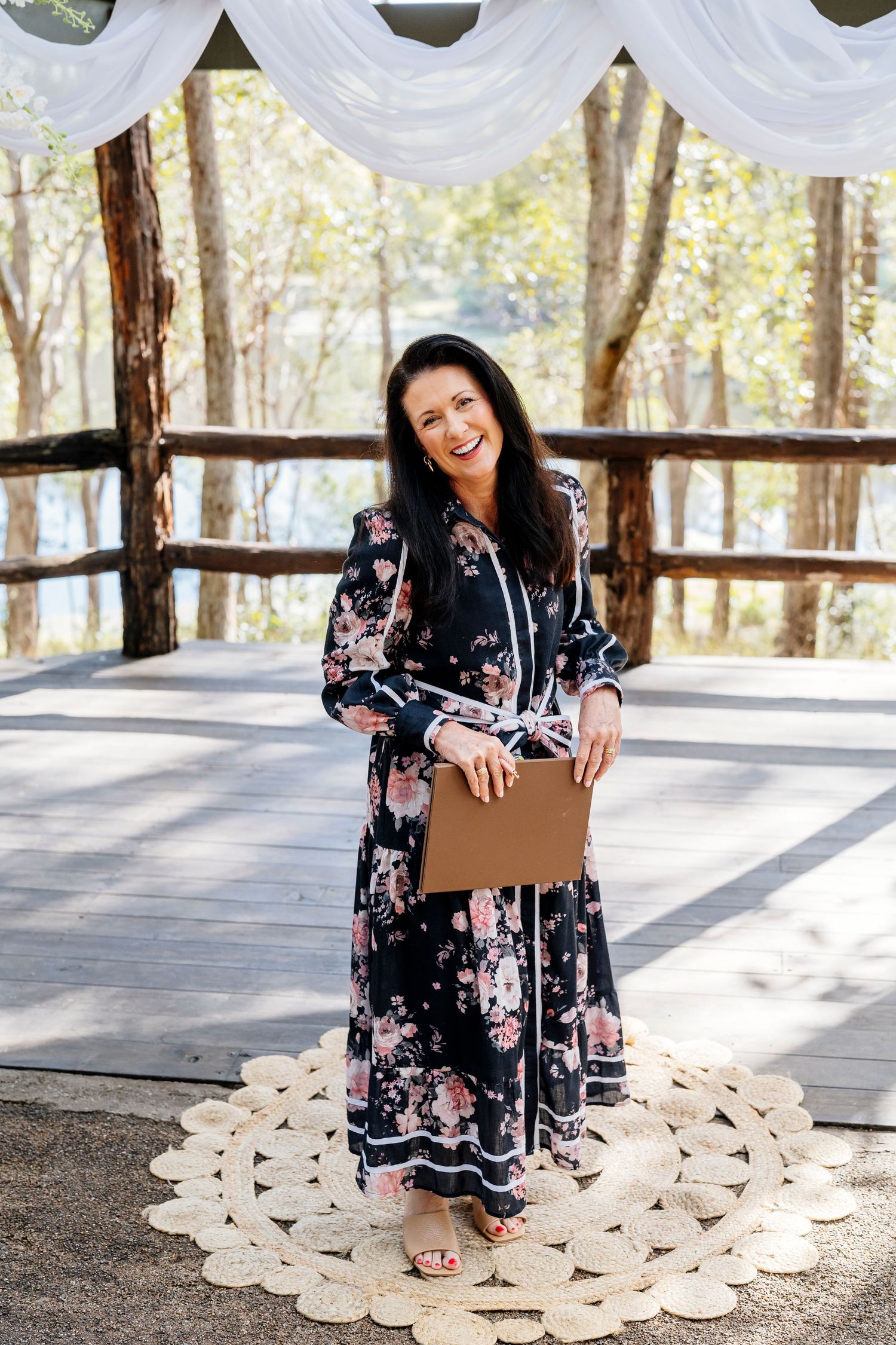 A person in a floral dress sits on a circular macrame rug in a rustic outdoor pavilion setting.