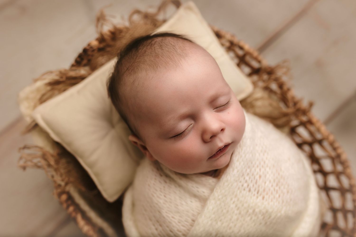 Baby boy sleeps soundly wrapped in cozy neutrals and in a boho basket, captured by Charlottesville newborn and family photographer.