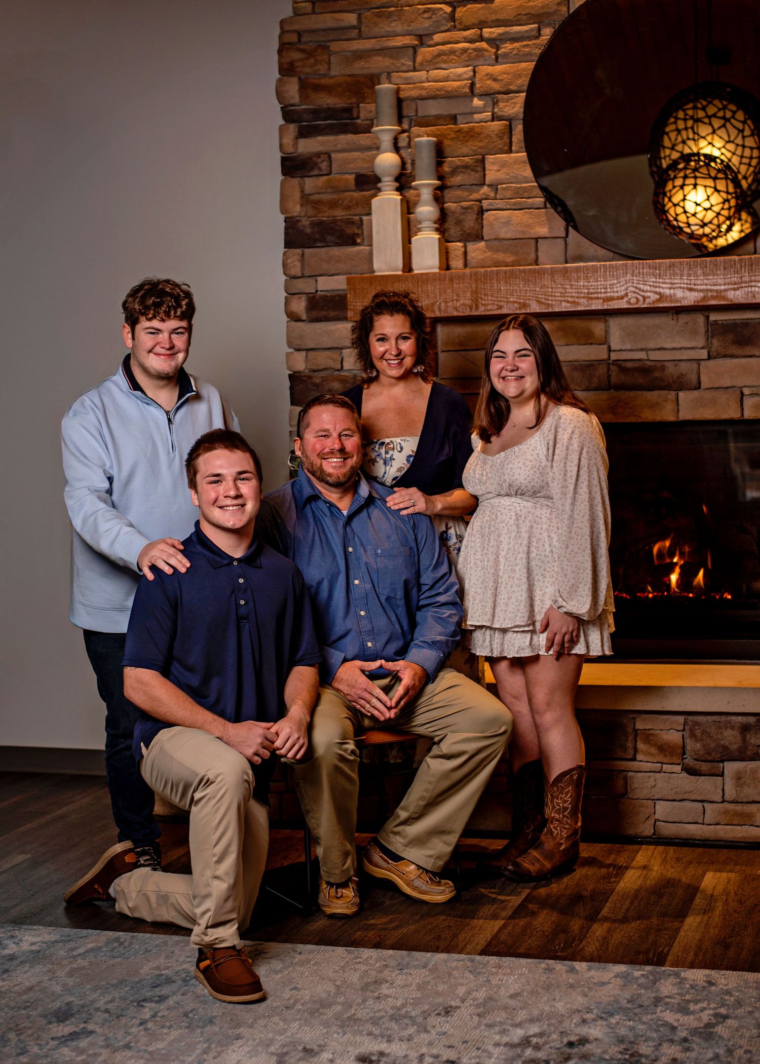 A group sits together on a wooden floor against a stone wall with warm lighting in a cozy indoor setting.