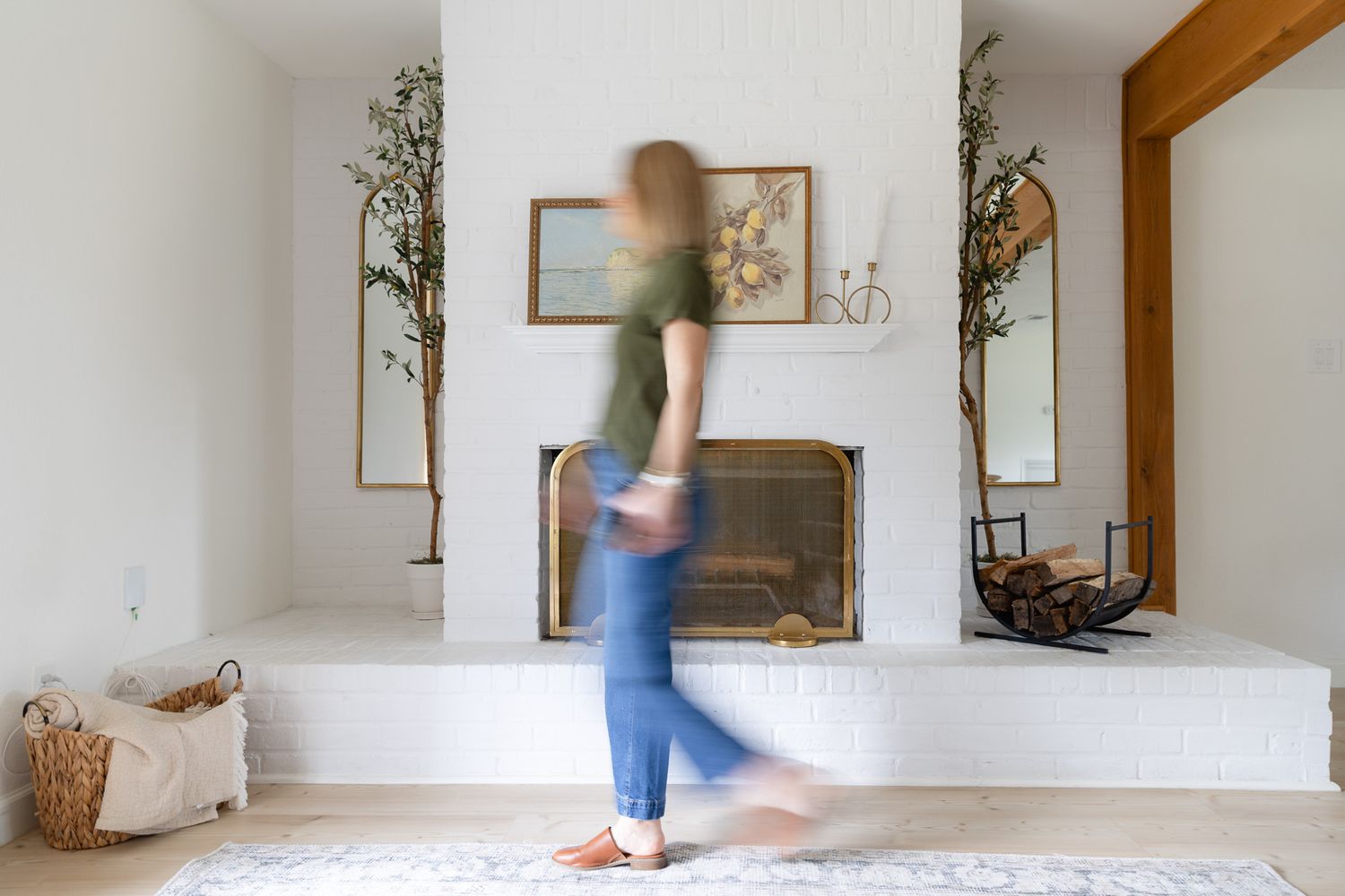 A blurred motion figure walks past a white fireplace with rustic decor and wooden accents in a minimalist living room Spring Texas