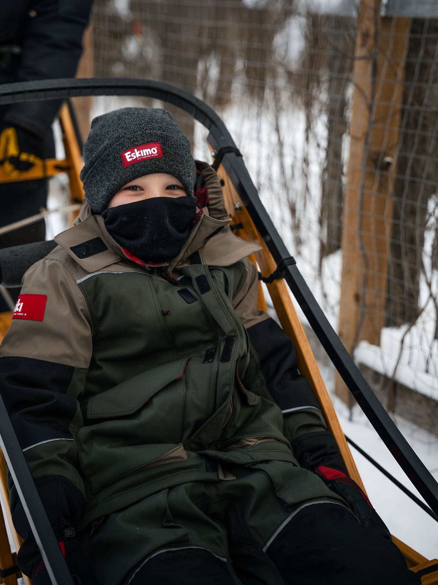 Bundled passengers riding in a dog sled through a snowy winter forest.