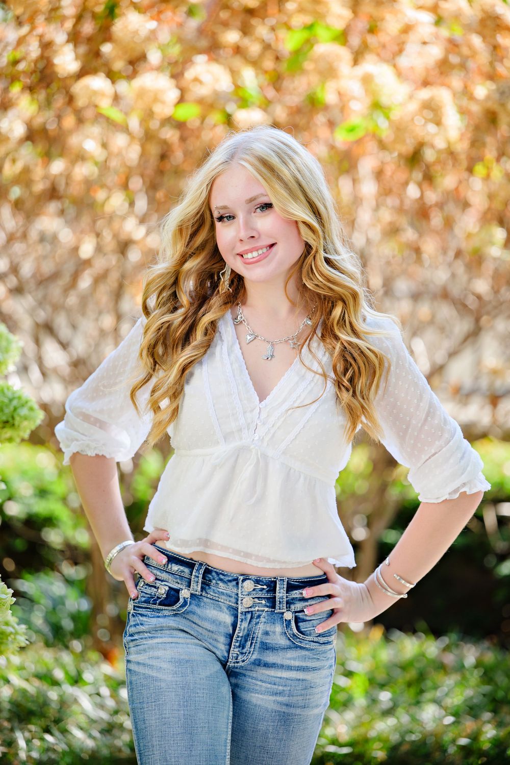 A high school senior girl wearing a white blouse and blue jeans against a natural autumn backdrop in Columbus Ohio