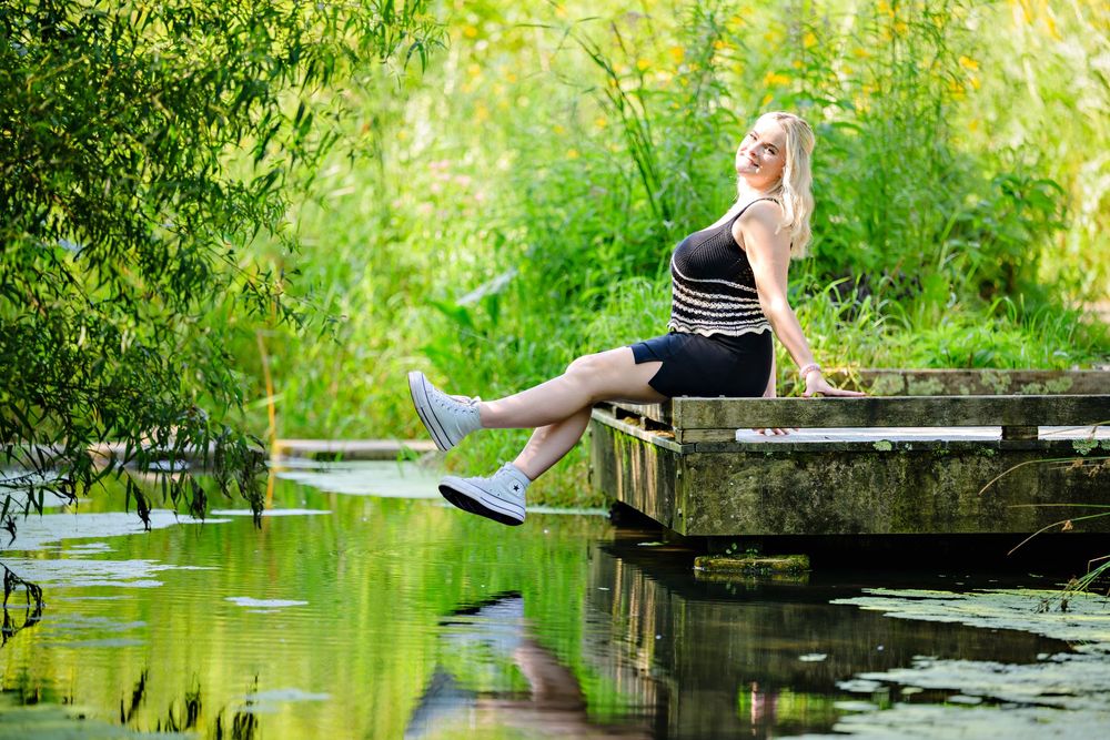 A high school senior girl sitting on a wooden dock by a tranquil pond surrounded by lush greenery at Inniswood Metro Gardens in Columbus
