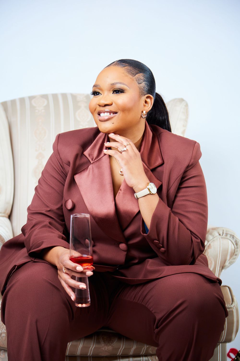 Stylish portrait session featuring person in burgundy suit on cream chair.