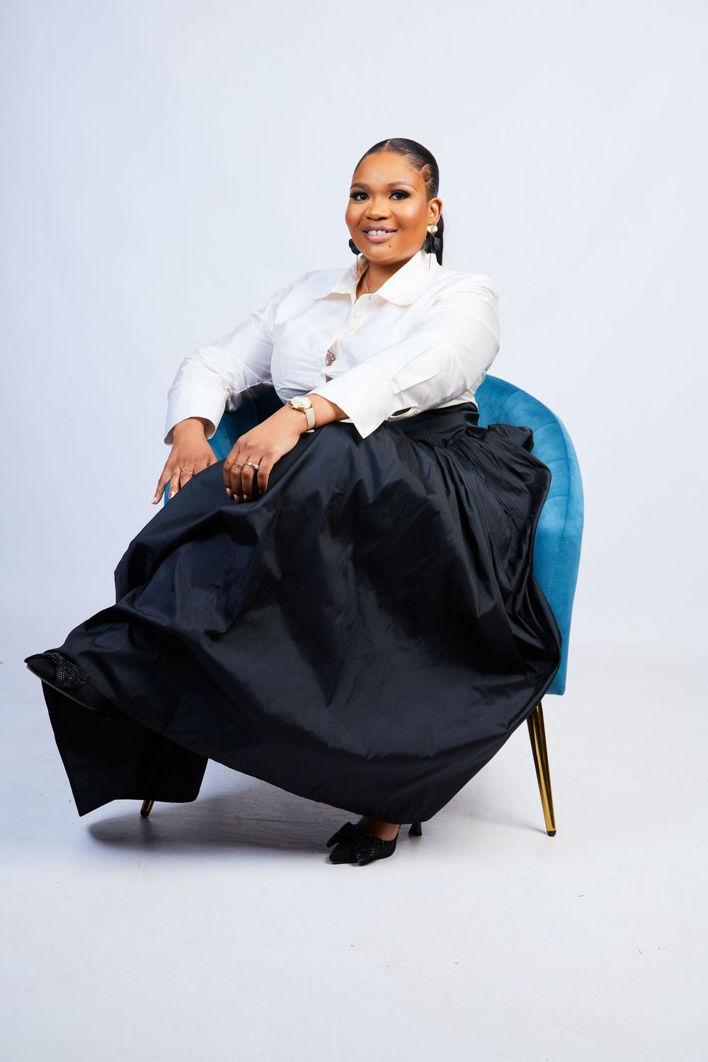 Fashion portraits of person in white top and black skirt on blue chair.